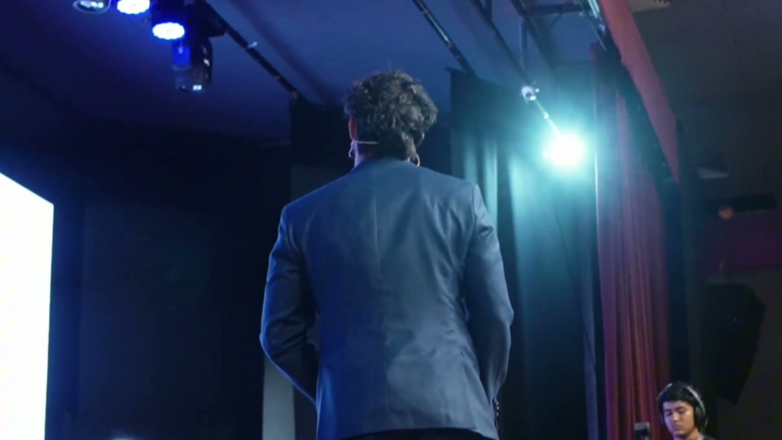 Frame da palestra de Jhon, blazer azul no palco